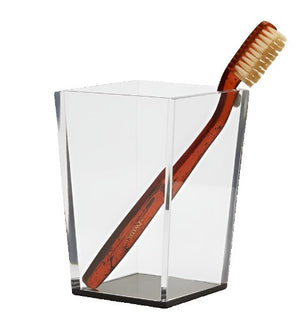 Part of the Pigeon and Poodle Monette Collection, a brown toothbrush with white bristles stands elegantly in a transparent, angular glass holder.