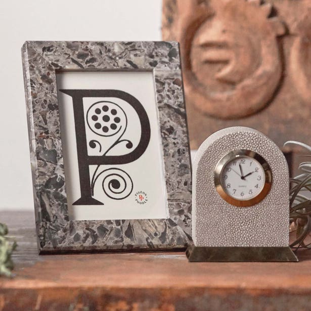 A Corsica Frame Collection piece with the letter "P" stands next to a small analog clock on a wooden surface.