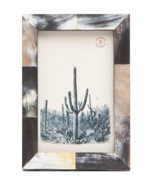 A rectangular Pigeon and Poodle Dark Horn Essen Frame, 4 x 6, with a patchwork pattern of earthy tones anchors this piece in the frame collection, displaying a black-and-white illustration of tall cacti in a desert landscape.