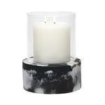 A white two-wick candle in a clear glass holder rests on the Milo Black Swirled Resin Hurricane, Large, from Pigeon and Poodle’s collection.