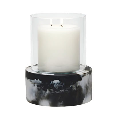 A white two-wick candle in a clear glass holder rests on the Milo Black Swirled Resin Hurricane, Large, from Pigeon and Poodle’s collection.