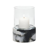 A white candle burns in the Milo Black Swirled Resin Hurricane, Small, featuring a clear glass insert set on a round, black-and-white marbled-resin base.