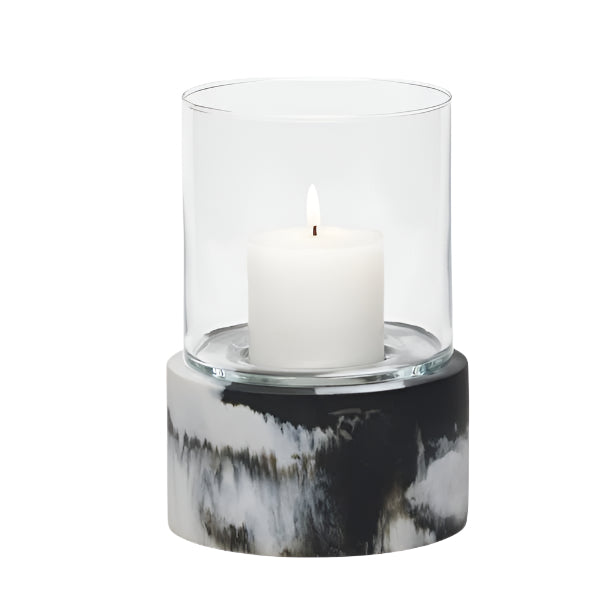 A white candle burns in the Milo Black Swirled Resin Hurricane, Small, featuring a clear glass insert set on a round, black-and-white marbled-resin base.
