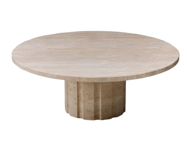 A round, beige marble table with a thick, cylindrical base featuring vertical grooves exudes timeless elegance. Its classical base highlights the raw travertine finish, creating a stunning centerpiece for any room.