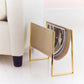 An AERIN Classic Croc Magazine Rack in Fawn, filled with magazines, sits on the floor beside a beige upholstered chair.