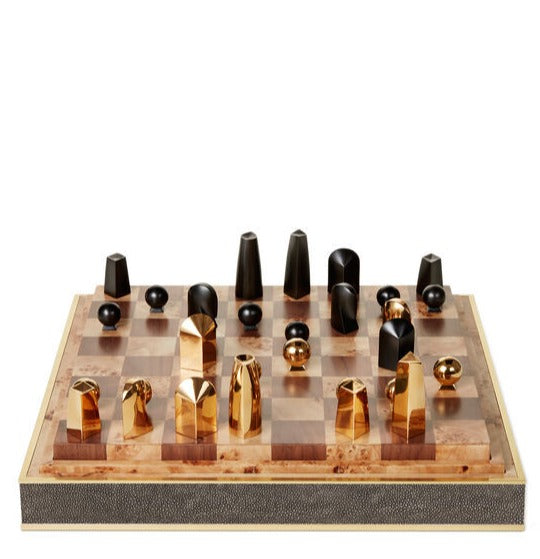 A luxurious AERIN Shagreen Chess Set with gold-plated and black pieces on a wooden board.