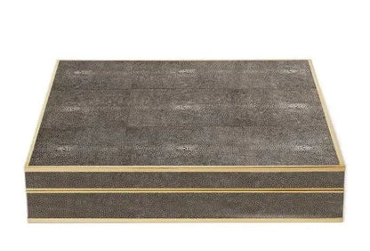 A stylish AERIN Shagreen Chess Set in a rectangular, textured box with a sleek, dark grey patterned surface and golden edges.