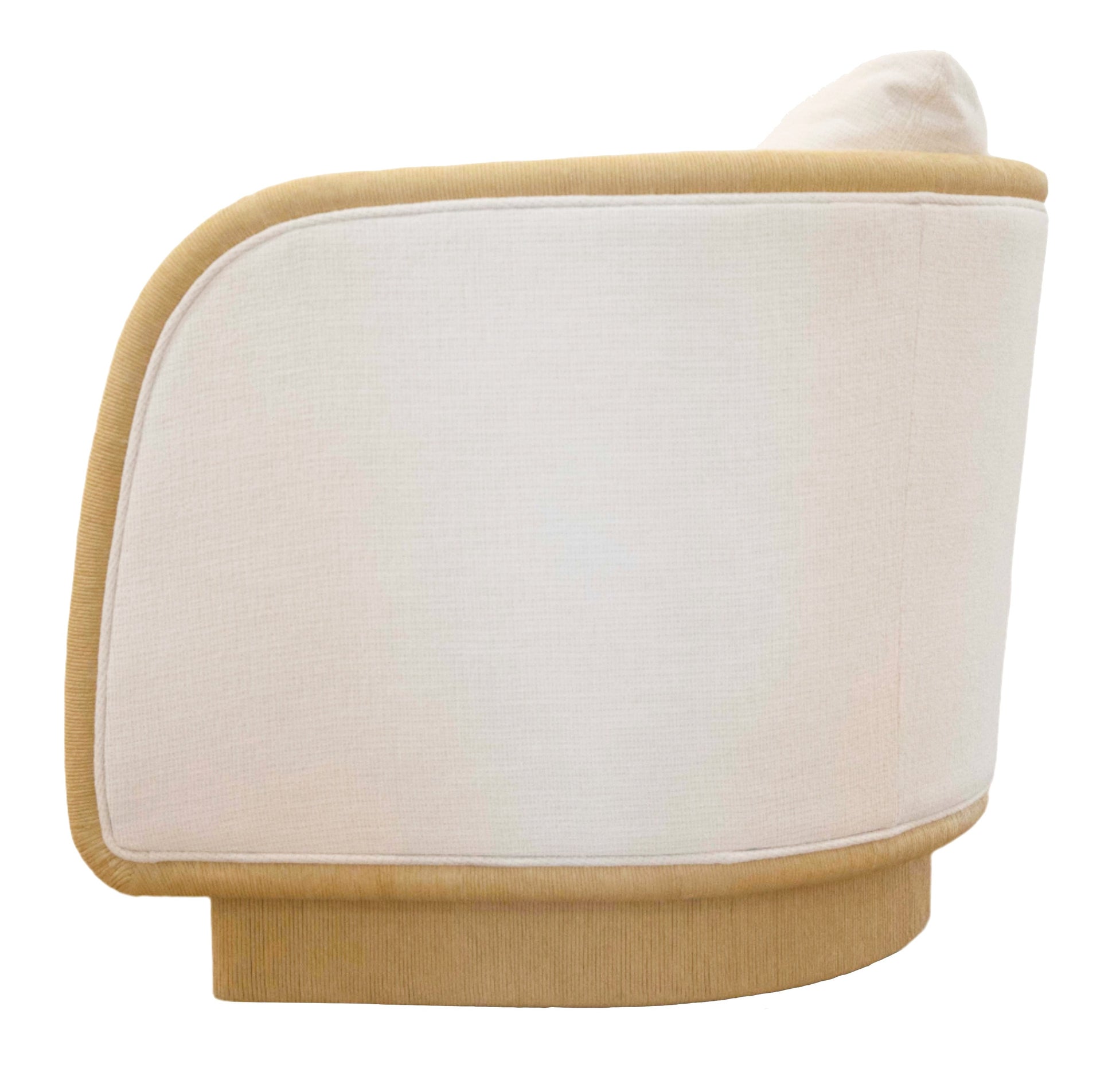 A beige, curved-back Coastal Swivel Chair with a light tan base and trim. Featuring a minimalist design, the chair appears to be upholstered in soft fabric, offering both style and comfort.