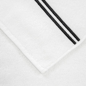 Close-up of a white bath towel from the Frette Classic Bath Collection, White/Grey, featuring highly absorbent cotton terry and black double border embroidery on one edge, laid on a matching white surface.