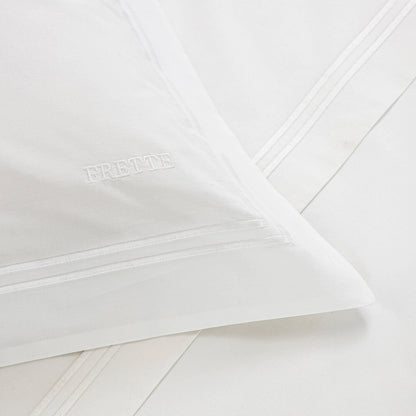 Close-up of a white Frette Classic Bedding Collection, White/White, featuring a simple border design and luxurious embroidered logo on the pillowcase.