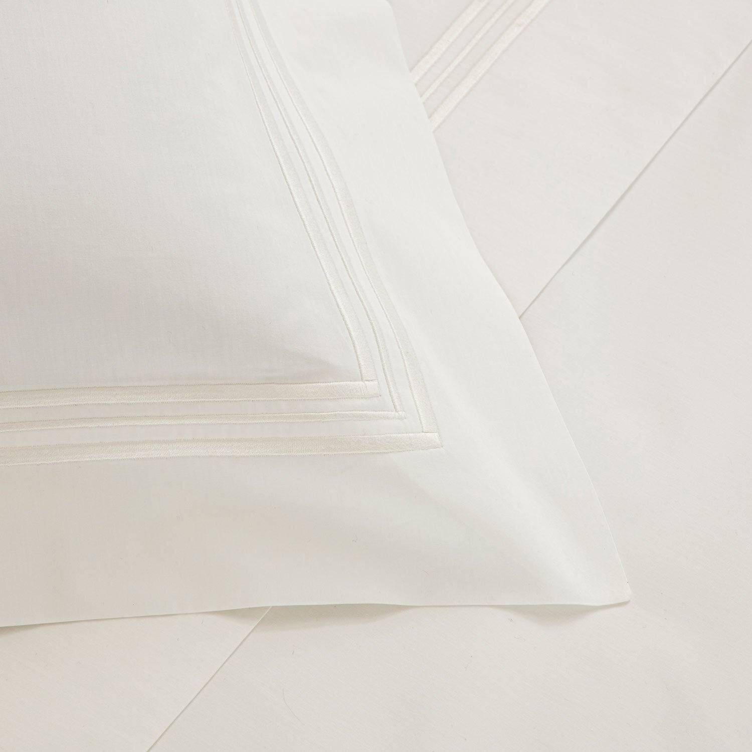 Close-up of a white pillowcase from the Frette Triplo Bourdon Bedding Collection, White/Milk, showcasing a crisp and clean appearance with smooth cotton poplin and an elegant three-line embroidery border detail.