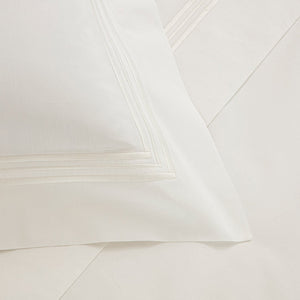 Close-up of a white pillowcase from the Frette Triplo Bourdon Bedding Collection, White/Milk, showcasing a crisp and clean appearance with smooth cotton poplin and an elegant three-line embroidery border detail.