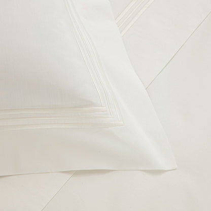 Close-up of a white pillowcase from the Frette Triplo Bourdon Bedding Collection, White/Milk, showcasing a crisp and clean appearance with smooth cotton poplin and an elegant three-line embroidery border detail.