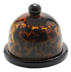 A dome-shaped, brown and black tortoiseshell pattern Blue Pheasant Andrew Butter Dish, Tortoise, crafted from durable hand-blown glass, features a knob on top and is placed on a round base.