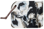 A rectangular abstract art piece with a leather strap attached, featuring swirling patterns in black and white with hints of brown. Perfect for those who appreciate mixed and matched functional pieces, this artwork brings an elegant touch to any space, much like the curated style of Blue Pheasant Noah Serving Board, Black.