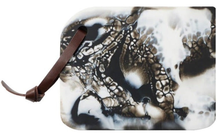 A Blue Pheasant Noah Serving Board, Black with a marbled black and white pattern and a brown leather strap looped through a hole in one corner, perfect for those who appreciate functional pieces that can be mixed and matched seamlessly.