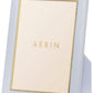 The AERIN Classic Piero Leather Frame Collection features a white photo frame with elegant gold detailing, standing upright. Inside, there is a placeholder displaying the text "AERIN" in gold letters.