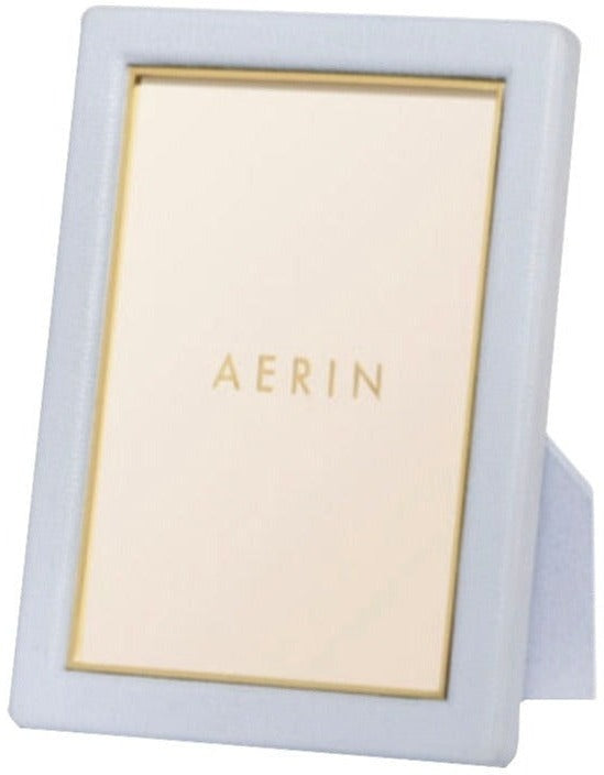 The AERIN Classic Piero Leather Frame Collection features a white photo frame with elegant gold detailing, standing upright. Inside, there is a placeholder displaying the text "AERIN" in gold letters.