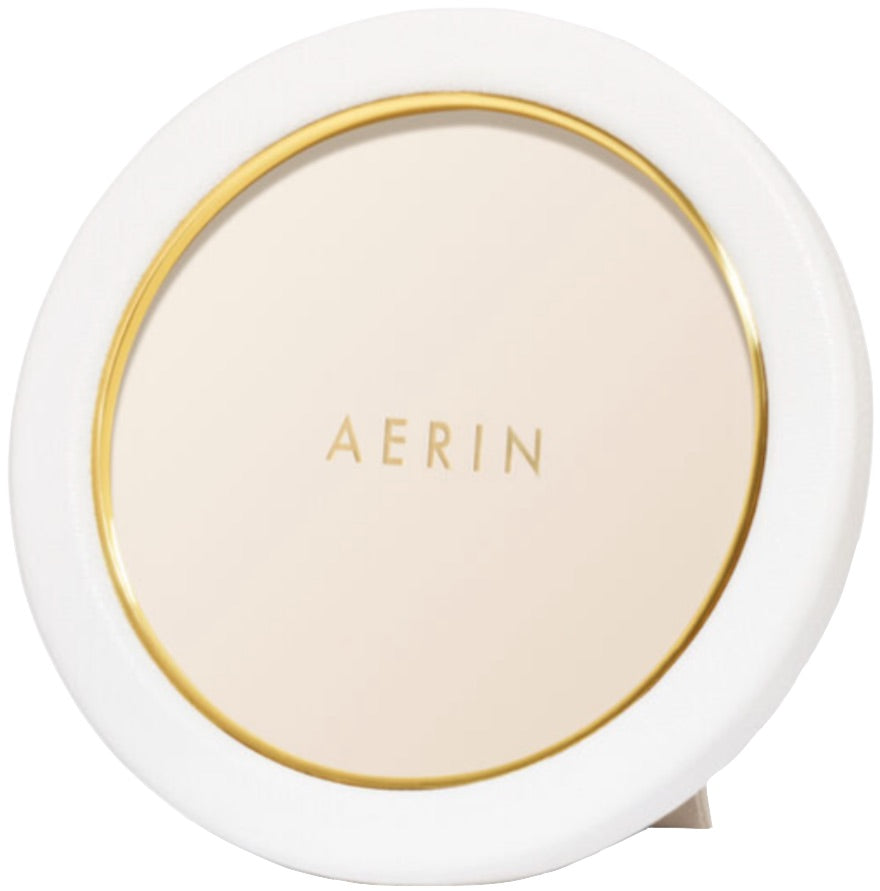 A compact powder with an elegant display, featuring a white and gold design labeled "AERIN Classic Piero Leather Frame Collection" on the lid.