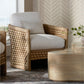 The Capitola Lounge Chair, featuring woven rattan and white cushions with a small pillow, sits beside a light wood coffee table and a vase of greenery against a patterned beige wall.
