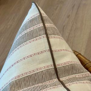A close-up of the Sifnos Peat Pillow, a handmade throw pillow featuring brown and pink stripes with brown piping, highlighting its superior craftsmanship, placed on a light wooden surface.