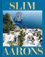 Cover of "Slim Aarons: The Essential Collection" book shows a seaside scene with people sunbathing on lounge chairs near the water, framed by rocky cliffs in the background. The book title is in large gold text, celebrating a comprehensive collection of Slim Aarons photography.