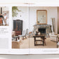 In "A Sense of Place," the open book showcases a modern living room with a stone fireplace, wooden furniture, and neutral decor, styled by designers Nate Berkus and Jeremiah Brent. The left page highlights their unique interior design approach and passion for travel.