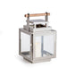 The Adwin Outdoor Lantern features a sleek chrome metal and glass design with a teak handle and holds an unlit white pillar candle inside.