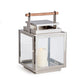 The Adwin Outdoor Lantern features a metal and glass design with a teak handle and houses a lit white pillar candle inside.