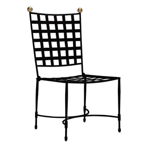 The Janus et Cie Amalfi Dining Side Chair in Slate features a black metal frame with a grid-patterned back and seat, accented by two gold spheres on the corners—an ideal outdoor piece with handcrafted details.