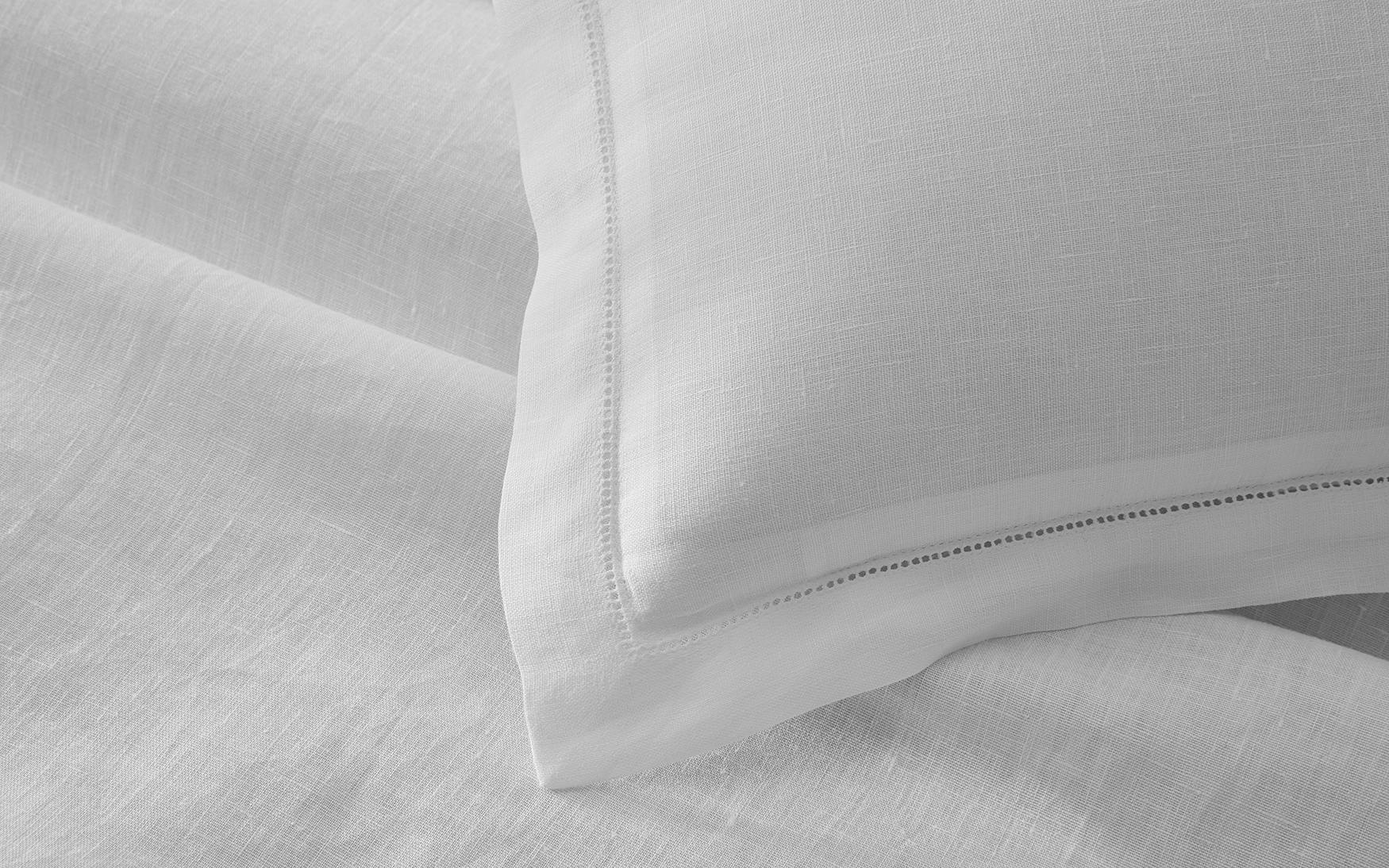 Close-up of a white pillow with hemstitch detailing, lying on Matouk Roman Linen Hemstitch Bedding Collection, White.