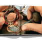 A person uses tools to work on an intricate timepiece. The image appears in an open book, showcasing a detailed view of the jewelry and craftsmanship involved, reminiscent of the Swiss-Italian watchmaking tradition seen in Bulgari Beyond Time.