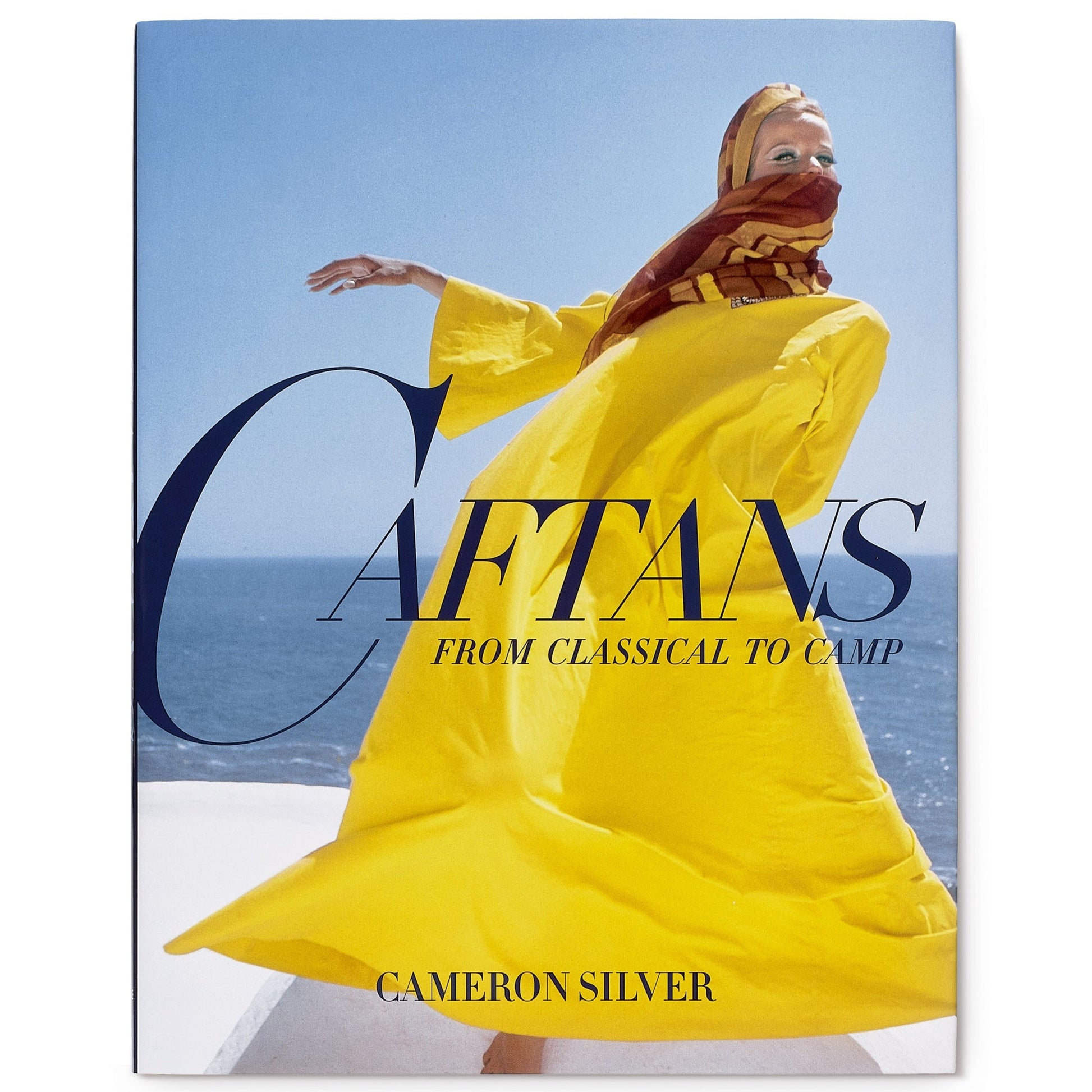 Cover of "Caftans: From Classical to Camp" by Cameron Silver, featuring a person in vibrant yellow caftan couture and patterned headscarf set against a blue sky and sea background.