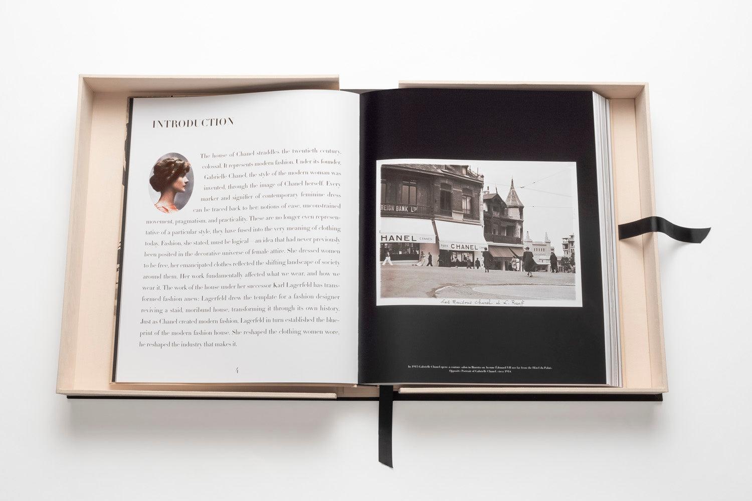 Open photo book with text on the left page and a black-and-white image of a storefront labeled "Chanel" on the right page, bound with a black ribbon bookmark, capturing the essence of luxury fashion and iconic looks in *The Impossible Collection: Chanel*.