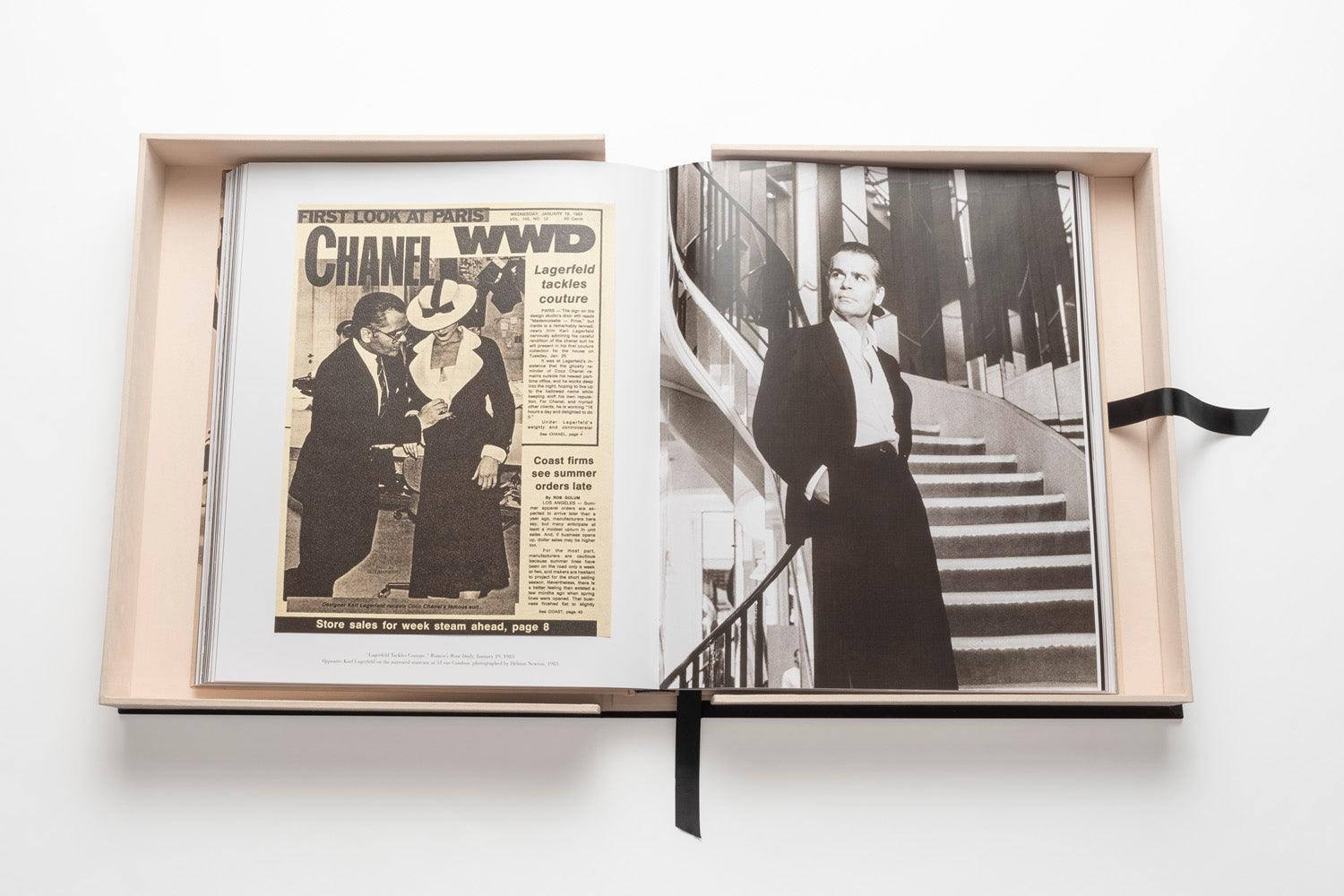 An open book shows a newspaper page featuring fashion designer Karl Lagerfeld in a black-and-white photograph, standing on a staircase in one of his iconic looks—a suit with a scarf. His contributions to The Impossible Collection: Chanel and luxury fashion are timeless and influential.