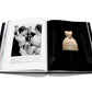 An open book displaying original photography by Laziz Hamani features a black-and-white photograph of two women talking on the left page and a Dior: Marc Bohan haute couture creation with a floral decoration on the right page.