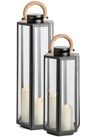 Two Napa Dockside Lanterns, crafted from black stainless steel and glass with natural teak wooden handles, each feature a lit white pillar candle.