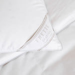 Close-up of a neatly-folded white bedding corner with a visible label reading "Frette Cortina Pillow Insert, Medium Density Made in Italy," revealing the luxurious sheen of cotton sateen, complemented by a fluffy pillow filled with Polish goose down.