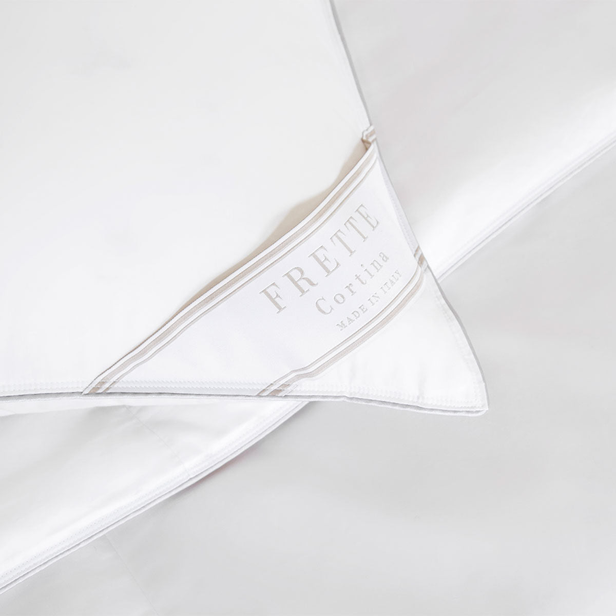 Close-up of white bedding with a Frette label that reads "Frette Cortina Made in Italy," nestled beside a Frette Cortina Pillow Insert, Firm Density made from luxurious Polish goose down.