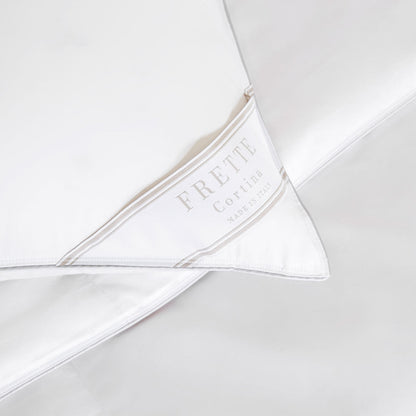 Close-up of white bedding with a Frette label that reads "Frette Cortina Made in Italy," nestled beside a Frette Cortina Pillow Insert, Firm Density made from luxurious Polish goose down.