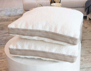 Two Neighbors Sheep Pillows with brown and white striped edges are stacked on a round white surface, crafted from the finest materials.