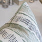 A close-up of a custom, down-filled Da Da Stripe Cactus Pillow from Associated Design, with a green and black abstract pattern, situated on a soft surface with blurred elements in the background.