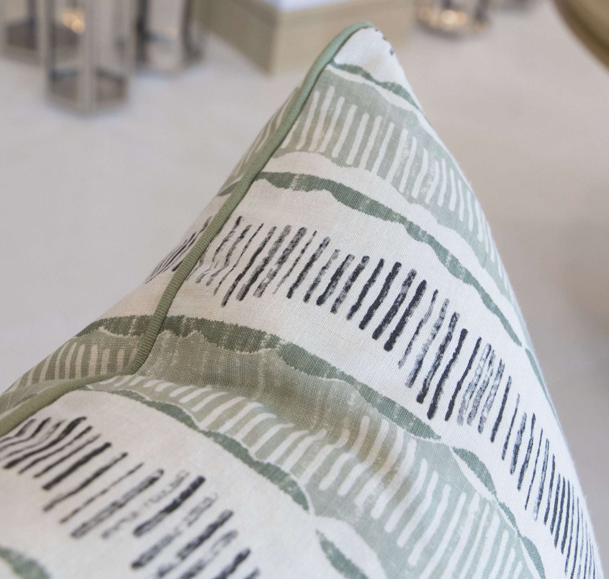 A close-up of a custom, down-filled Da Da Stripe Cactus Pillow from Associated Design, with a green and black abstract pattern, situated on a soft surface with blurred elements in the background.