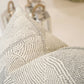 Close-up of a Maralinga Ombre Pillow with intricate dot designs, crafted from the finest materials. Two metallic lanterns with wooden handles are slightly out of focus in the background.