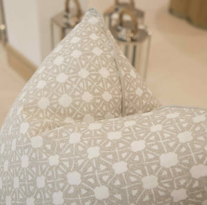 Close-up of the Seville Shale Pillow, featuring a geometric white and beige pattern made from premium materials, with blurred metallic decor in the background.