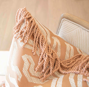 Close-up of the Tigres Peche Pillow, showcasing beige and white geometric patterns with fringed trim on a wooden chair, crafted from premium materials inspired by the Kips Bay Show House.