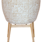 The Coupe Chair features a modern design with white and gold geometric-patterned fabric. Its mid-century style is complemented by light wooden legs adorned with gold accents at the tips.