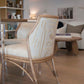 A modern Lantana Side Chair with wooden legs and patterned upholstery stands next to a glass table in a cozy living space, showcasing Lantana Side Chair craftsmanship. In the background, you can see a sofa, coffee table, and bookshelves.