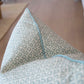 Close-up of the Zeimoto Dove Pillow, a custom-made accent pillow in light blue and white with geometric and floral motifs and piped edges, shown against a blurred background.