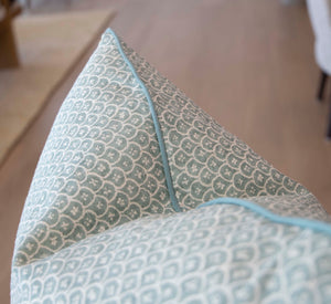 Close-up of the Zeimoto Dove Pillow, a custom-made accent pillow in light blue and white with geometric and floral motifs and piped edges, shown against a blurred background.